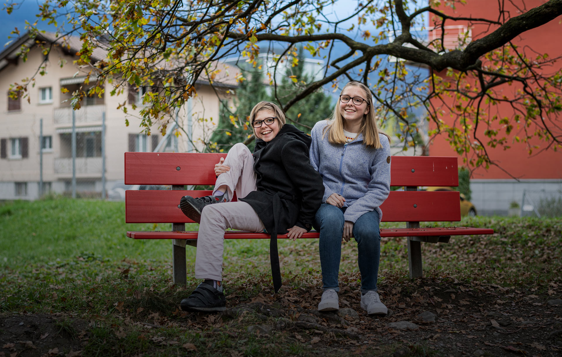 Zwei junge Mädchen sitzen auf einer roten Bank und haben Spass miteinander